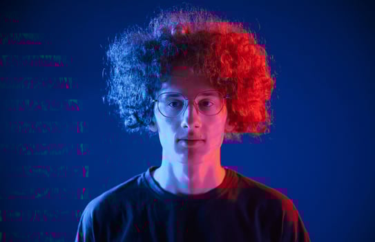 Serious facial expression.. Young man with curly hair is indoors illuminated by neon lighting photo