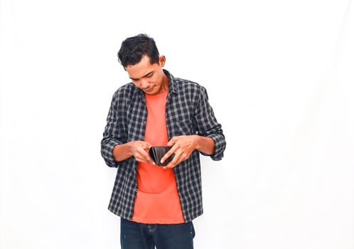 Young Man In Casual Attire Examining Wallet Against Plain Background photo