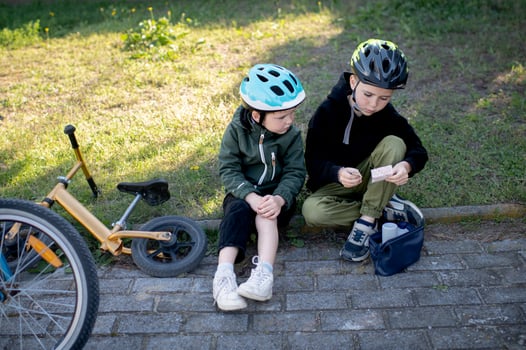 Two boys cyclists wearing helmets are taking a break one is applying a band aid to his scraped knee from a first aid kit photo