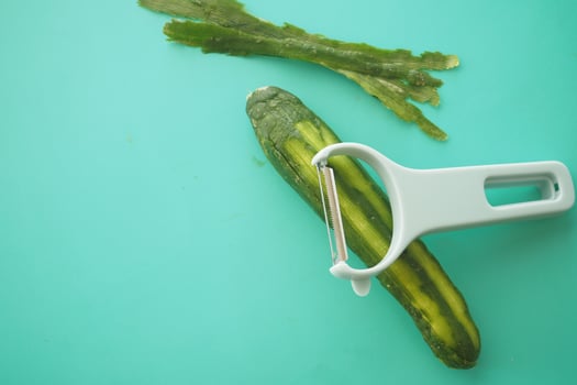 Peeling a cucumber on a turquoise cutting board in a kitchen photo