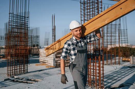 Holding big wooden ,,piece. Man is working on the construction site at daytime photo