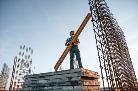 In grey uniform.. Holding wooden plank. Man is working on the construction site at daytime photo