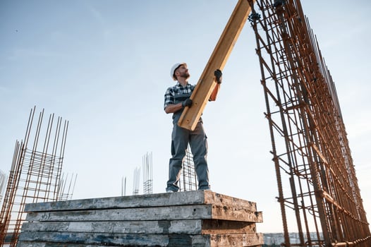 In grey ,uniform.. Holding wooden plank. Man is working on the construction site at daytime photo
