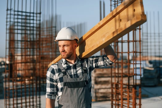 Man is working on the construction site at daytime. With wooden plank photo