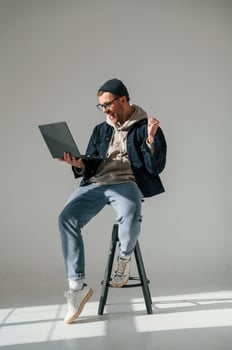 In casual clothes. With laptop. Sitting ,on the chair. Handsome man is in the studio against white background photo
