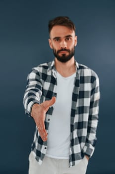 Giving, a hand, greetings. Handsome man is in the studio against blue background photo