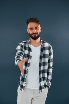 Giving a hand, greetings.. Handsome man is in the studio against blue background photo
