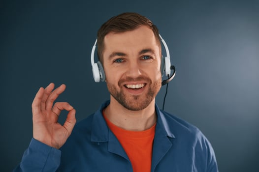 Showing fine, okay, good, sign., Smiling. In headphones. Handsome man is in the studio against blue background photo