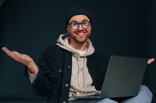 Smiling, sitting and using laptop. Handsome man is in the studio against background photo