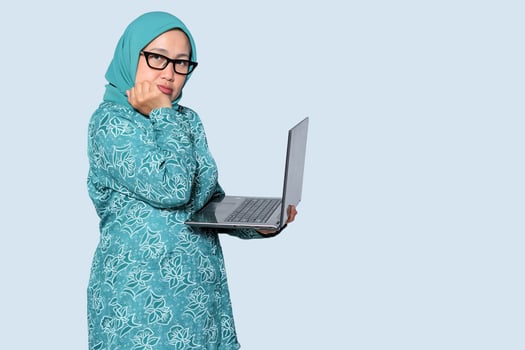 Frustrated Muslim business woman holding a laptop, expressing stress. Ideal for work, technology, and career challenges concepts photo