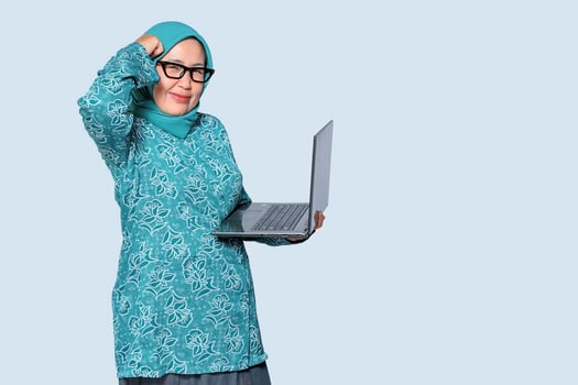 Confused Muslim business woman holding a laptop, expressing frustration. Ideal for work, technology, and career challenges concepts photo