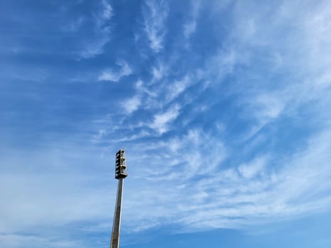 A searchlight lighting mast against the background of a blue sky with feathery clouds photo