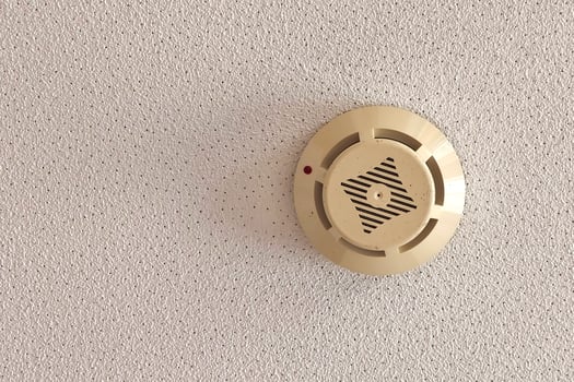 A smoke detector is mounted on the ceiling of a living space, functioning as a crucial safety device to detect fire hazards. It features a circular design with a grill and indicator light. photo