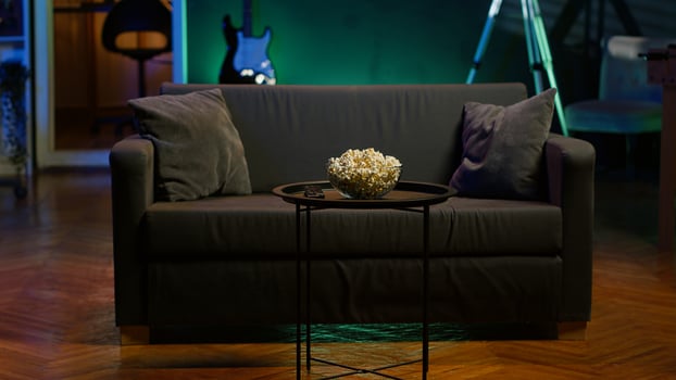Cozy residential interior with sofa and snacks, ready for casual movie night or immersive TV viewing experience. Bowl of popcorn on table in neon illuminated home theater apartment photo
