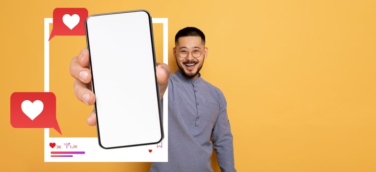 A smiling influencer holds a smartphone in front of a plain yellow background, showcasing a blank screen ready for social media interactions, expressing excitement and engagement online. photo