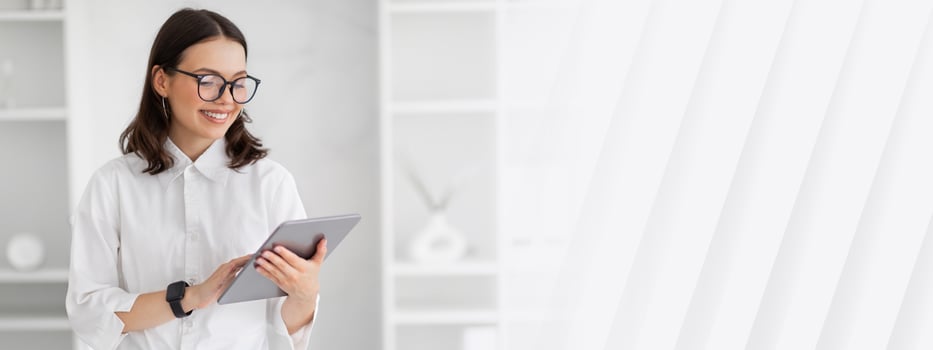 Positive millennial european business lady in glasses uses tablet to chat, enjoy work in white office interior. Modern lifestyle, app for business, technology for startup, investments photo