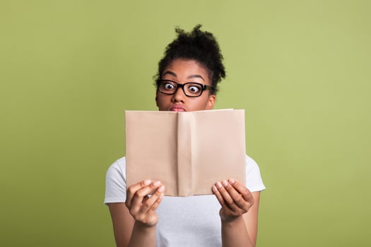 Education Concept. Amazed young black woman wearing glasses reading book on green studio wall, copy space photo