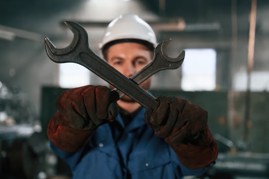 Holding two, wrenches. Factory, worker in blue uniform is indoors photo