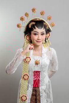 A Indonesian bride in Solo Putri attire, wearing a golden headdress and jasmine garland. She poses with a gentle smile and a raised fist, symbolizing confidence, elegance, and cultural pride. photo