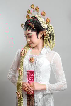 Elegant Indonesian bride in Solo Putri traditional attire, wearing a golden headdress, jasmine garlands, and intricate lace kebaya, radiating grace with a warm smile. photo