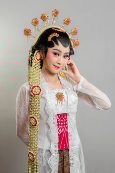 Indonesian bride in Solo Putri attire, wearing an intricate golden headdress and lace kebaya. She gently touches her ear while smiling softly, radiating elegance and grace. photo