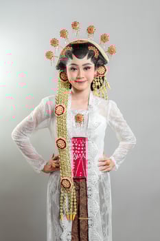 An Indonesian bride in Solo Putri attire, wearing a golden jasmine headdress, white lace kebaya, and batik. She smiles warmly with confidence, showcasing Javanese cultural elegance. photo