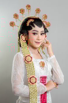 A Indonesian bride in Solo Putri attire, wearing an intricate golden and jasmine headdress, white lace kebaya, and red jewelry, smiling gracefully with a confident expression. photo