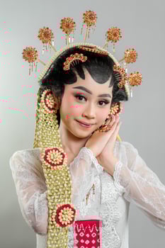 A Indonesian bride in Solo Putri traditional attire poses gracefully. She wears an intricate golden headdress, jasmine accessories, and a white lace kebaya, showcasing elegance with a soft smile. photo