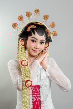An Indonesian bride in Solo Putri traditional attire poses gracefully. She wears an intricate golden headdress, jasmine accessories, and a white lace kebaya, showcasing elegance with a soft smile. photo
