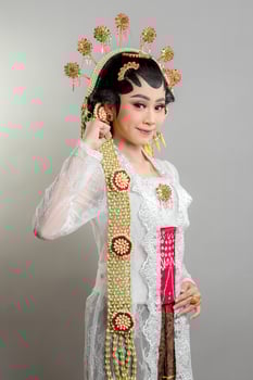 Indonesian bride in Solo Putri attire, wearing a golden headdress and jasmine garland. She poses with a soft smile and confident gesture, radiating elegance and tradition. photo