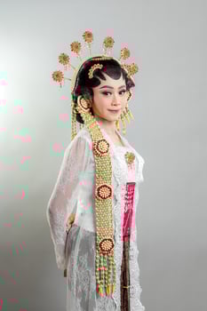 An Indonesian bride in Solo Putri attire wearing a golden jasmine headdress and white lace kebaya. She poses gracefully with a soft smile, showcasing Javanese wedding elegance. photo