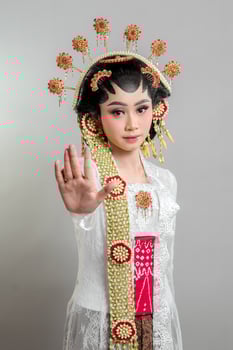 a Indonesian bride in Solo Putri attire, wearing a lace kebaya and ornate headdress. She gazes confidently, extending her hand in a stop gesture, exuding elegance and grace. photo