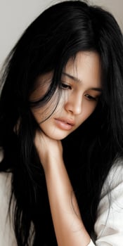 Pensive young Asian woman with long black hair looking down photo