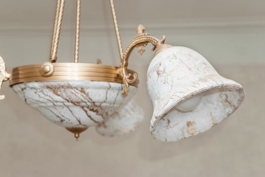 Image of a vintage chandelier with ornate marble shades, captured in a broken state. The delicate design features elaborate metalwork and intricate artistry, highlighting its antique charm photo