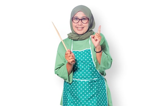 Cheerful Muslim woman chef wearing an apron, holding a wooden spatula, and smiling. Perfect for cooking, culinary, and home lifestyle themes photo