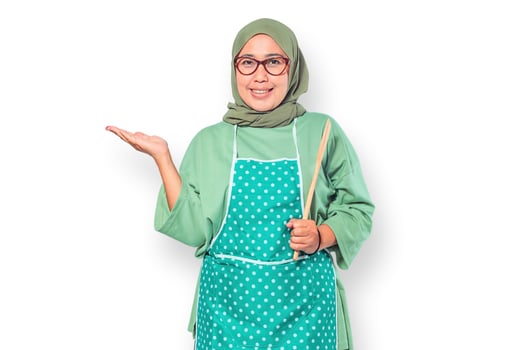 Smiling Muslim woman wearing an apron holding a wooden spoon ready to cook photo
