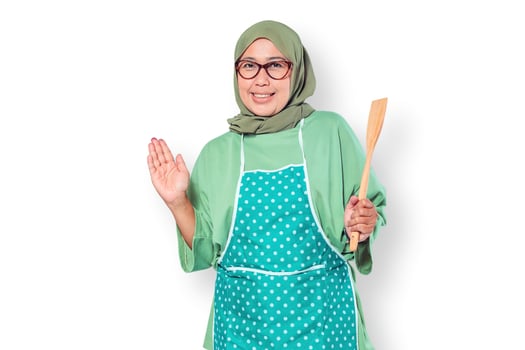 Cheerful Muslim woman chef wearing an apron, holding a wooden spatula, ready to cook in the kitchen photo