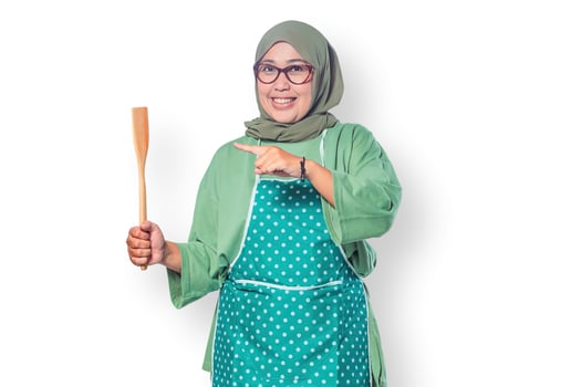 Happy Muslim woman in an apron holding a wooden spatula, symbolizing home cooking, passion for food, and a warm kitchen atmosphere photo