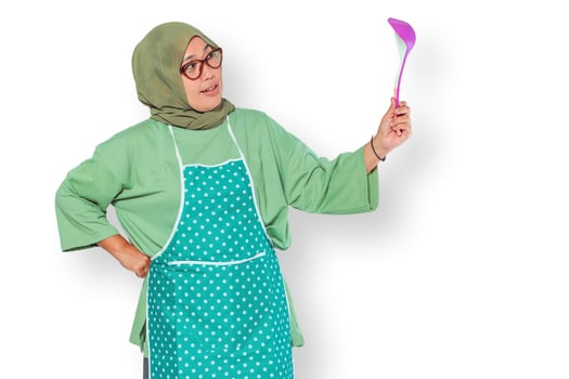 Muslim woman wearing an apron holding a ladle, posing confidently in the kitchen photo