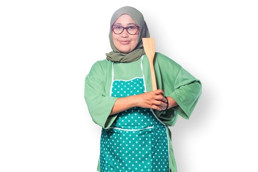 Confident Muslim woman in a hijab and apron holding a wooden spatula in the kitchen photo