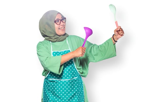 Happy Muslim woman wearing a hijab and apron joyfully cooking with ladles in the kitchen photo