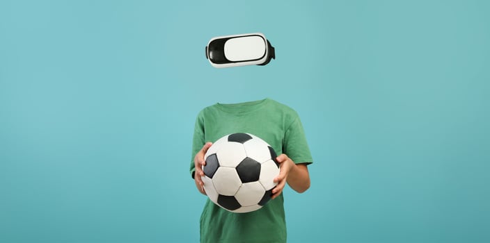Wearing a virtual reality headset, a person is engaged in an immersive experience while holding a soccer ball. The minimalist background enhances the focus on the gadget and the activity. photo
