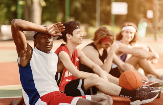 Tired black basketball player resting with his diverse team at sports court outside photo