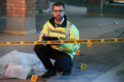 Male detective i,s collecting, evidence in a crime scene near dead body on the construction site. Sitting with notepad in hands photo