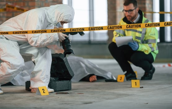 Woman is making photos by camera. Detectives are collecting evidence in a crime scene near dead body