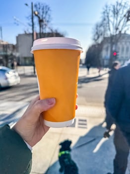 Hand Holding Takeaway Coffee Cup on City Street, Sunny Day, Urban Lifestyle, Beverage, Outdoor Scene. High quality photo