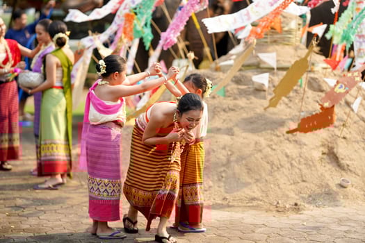 Group of Thai children's with beautiful Thai young woman and in the Thai traditional dress playing human cave train on outdoor pile of sand in Songkran festival. photo
