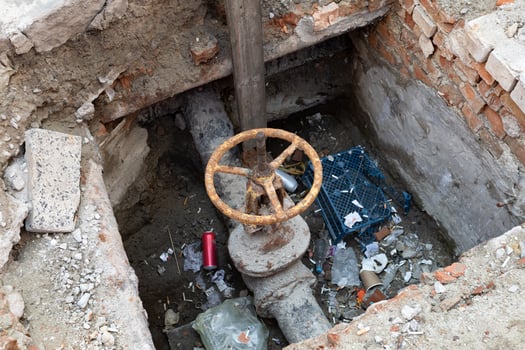 A rusty valve surrounded by trash sits in a decaying, dirty pit in an urban environment. photo