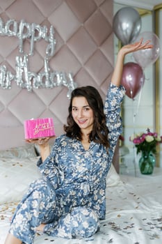 Woman celebrating birthday with cake and balloons in bedroom photo
