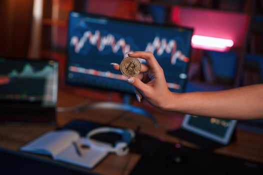Close up view ,of woman's hand that holding bitcoin against computer display and tablet with graphs photo